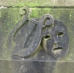 carved lyre harp and theatre mask carved on to cemetery gravestone